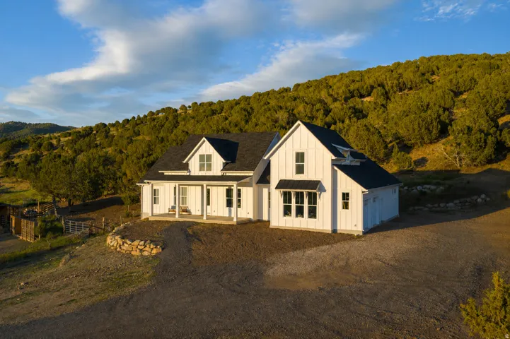 Modern farmhouse exterior featuring white vertical siding, black shingle roof, covered front porch, multiple gables, and an attached garage
