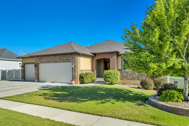Stone and stucco exterior with a multi-car garage, mature landscaping, and a retaining wall