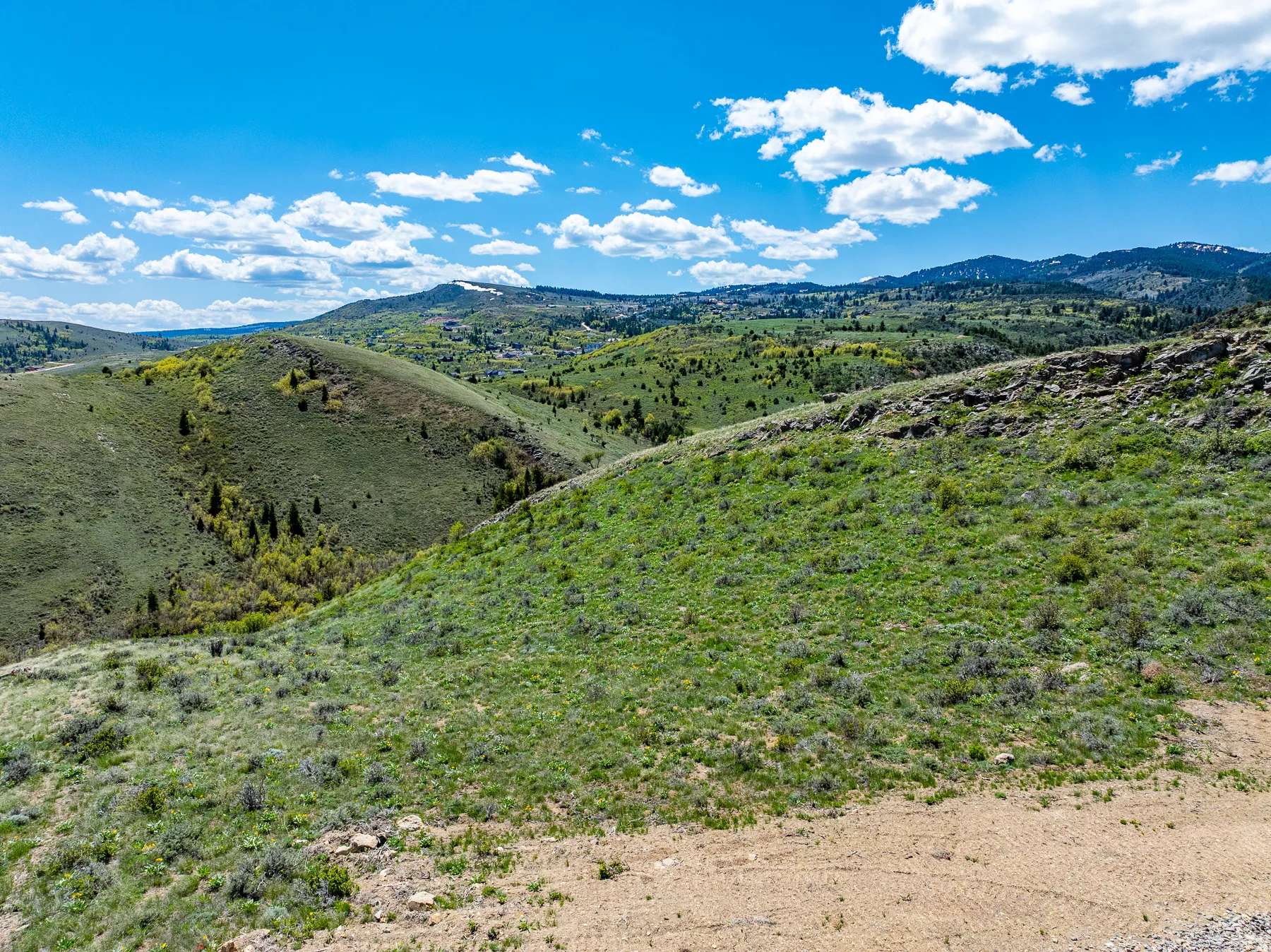 Expansive land parcel featuring undulating hills, verdant ground cover, and distant mountainous terrain