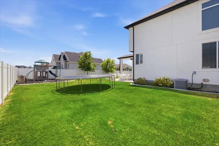 Expansive backyard featuring a large lawn, white privacy fencing, and a covered patio area