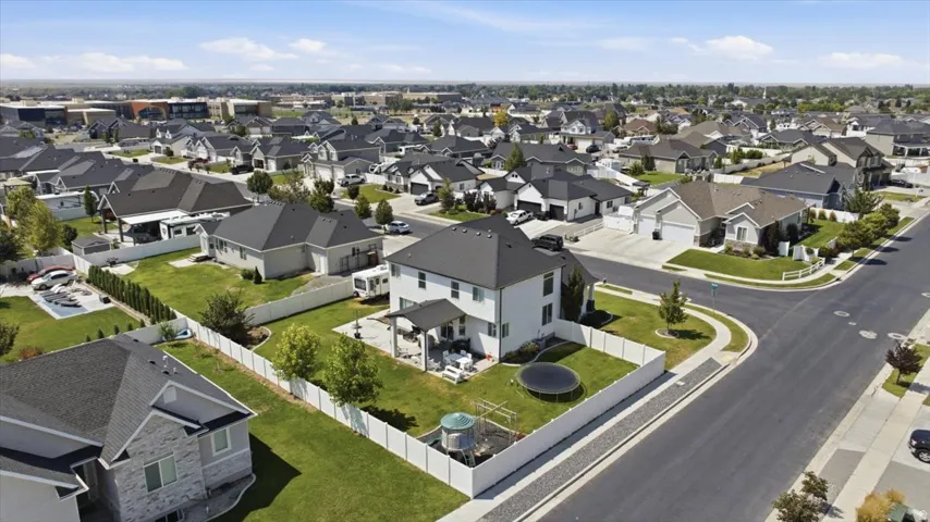 Aerial view showcasing a two-story residence with a dark-pitched roof and light-colored exterior siding, situated on a corner lot with manicured lawn, mature landscaping, and defined hardscaped borders