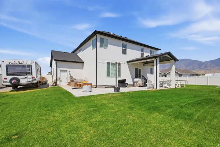 Modern two-story home with clean-lined exterior, featuring a covered rear porch, expansive manicured lawn, and mountain backdrop
