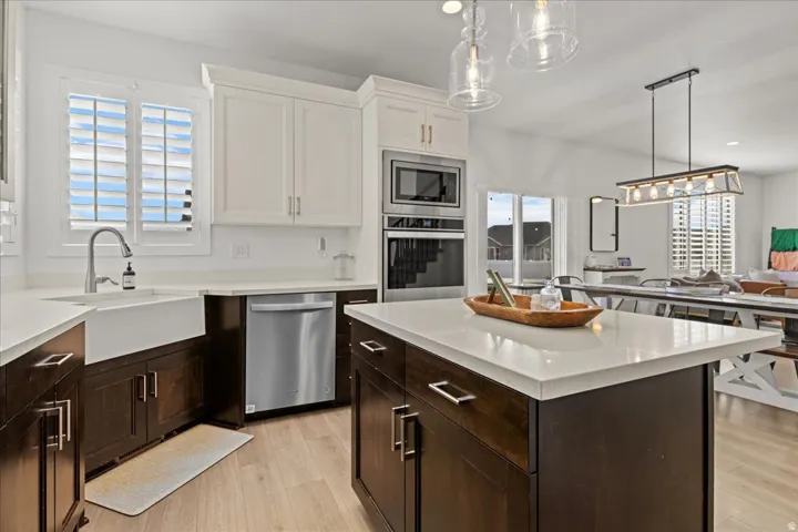 Contemporary kitchen featuring a large center island with a light-toned countertop, wood-finish flooring, two-tone cabinetry, stainless steel appliances, and a farmhouse sink