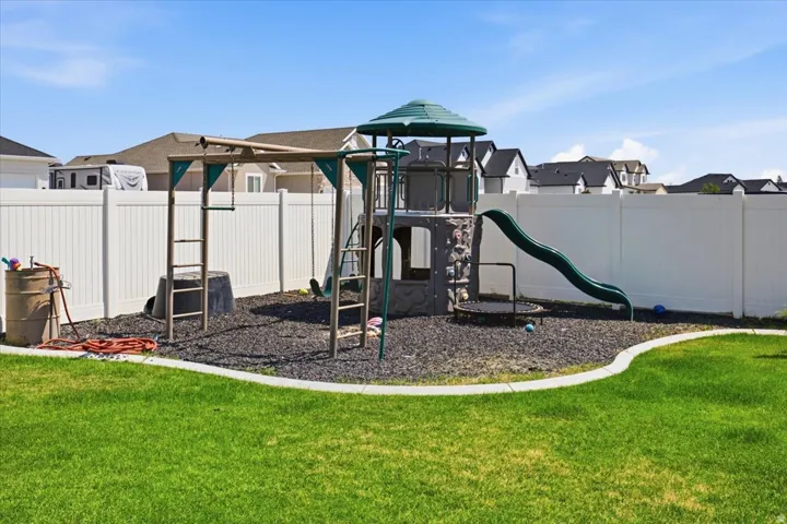 Expansive backyard featuring a manicured lawn, white privacy fencing, and a built-in play structure with a slide and swings