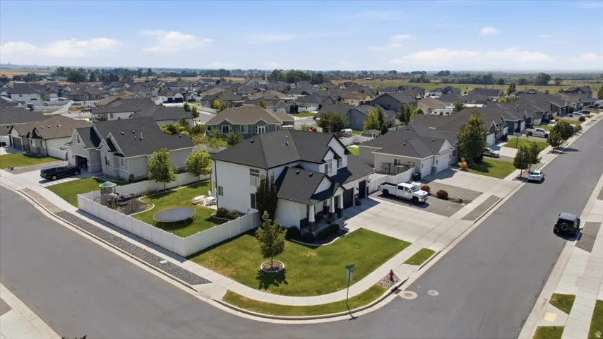 Corner lot property featuring a white privacy fence, manicured lawn, and a paved driveway