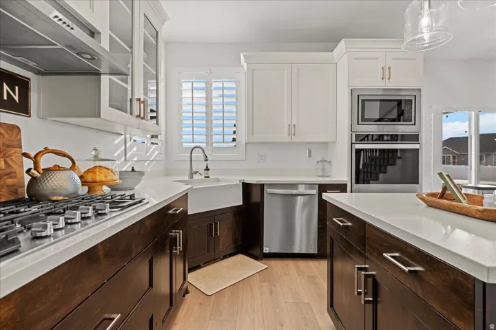 Gourmet kitchen featuring a gas range with stainless steel hood, built-in microwave and oven, apron front sink, and two-tone cabinetry with an island workspace
