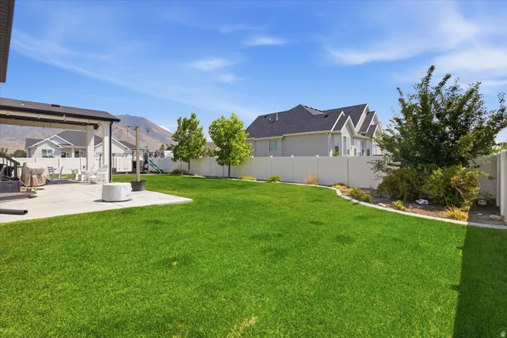 Expansive backyard featuring a meticulously manicured lawn, mature landscaping with established trees and shrubs, and mountain backdrop