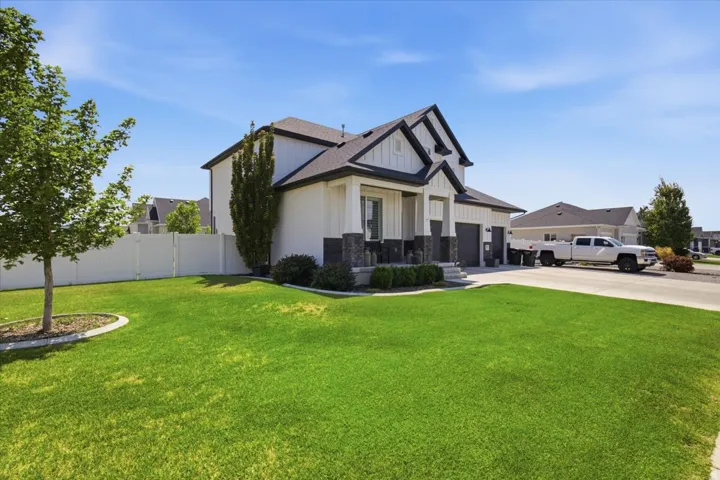 Modern farmhouse exterior with white vertical siding and dark gray stone accents, featuring a deep front porch and a two-car garage