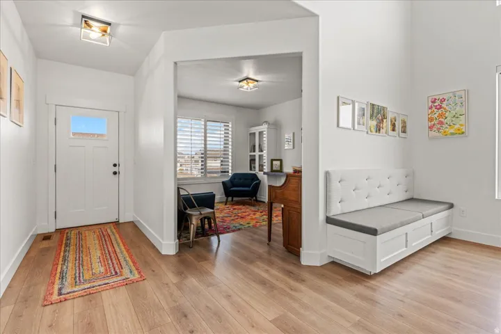 Entryway featuring wood-finish flooring, a white paneled entry door with an upper window, and a built-in bench with upholstered back and seat cushions