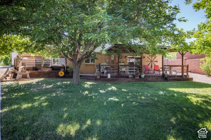 Expansive lawn area featuring a large mature tree, a multi-level wood deck, and a covered patio area