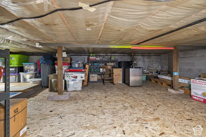 Utility basement space featuring exposed wood-finish floor joists, block wall construction, and a plywood subfloor