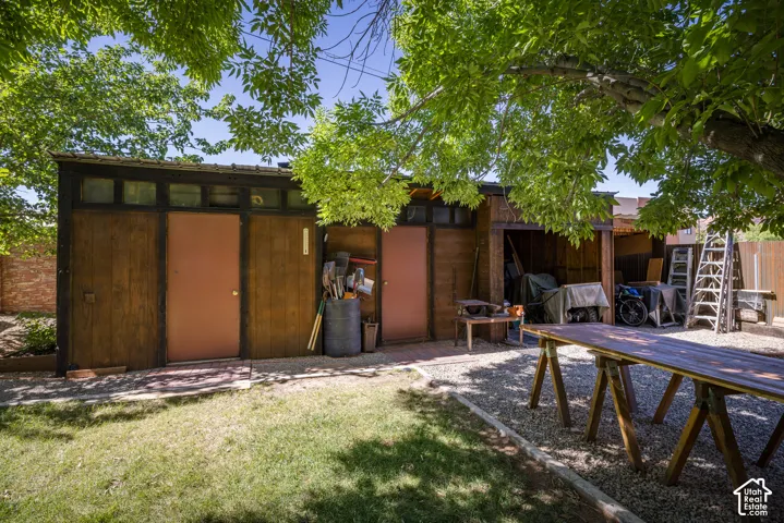 Backyard featuring a wooden utility structure with multiple entry points and transom windows, a gravel-covered area, and a section of manicured lawn