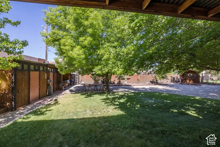 Expansive outdoor space featuring a lush lawn, mature trees, gravel ground cover, a wooden shed, and a privacy fence
