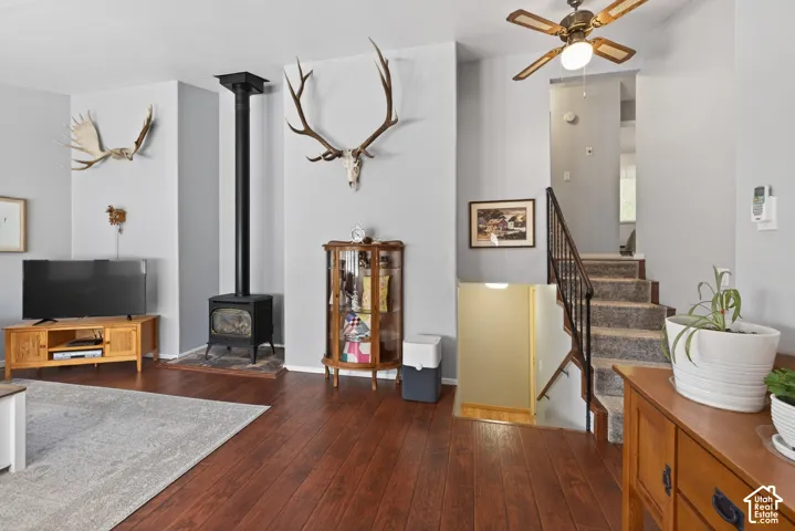 Living area featuring wood-finish flooring, a black cast iron wood-burning stove with a stovepipe, and a carpeted staircase with a dark metal railing