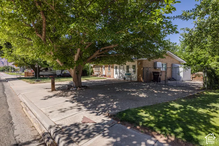 Brick exterior with a mature shade tree, gravel driveway, chain-link fence, and a concrete sidewalk