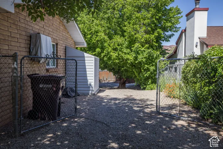 Gravel side yard featuring a chain-link fence, brick exterior, and a detached storage shed