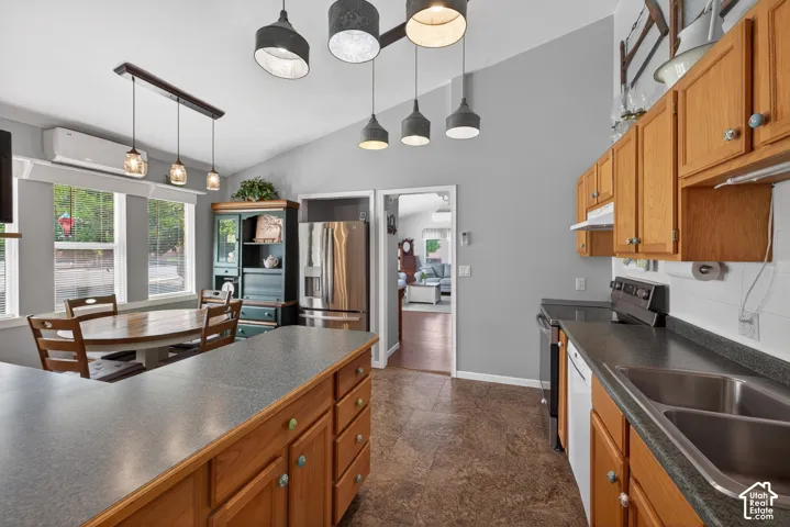 Open-concept kitchen with vaulted ceilings, featuring wood cabinetry, stainless steel appliances, and a double basin sink
