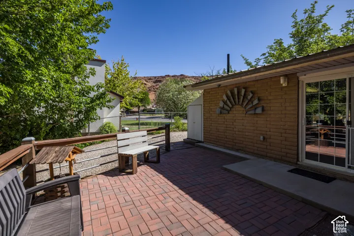 Brick paver patio featuring a sliding glass door entry, a light brick exterior wall, and a raised wooden deck with a cable railing