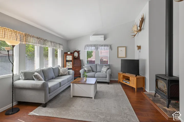 Living area featuring wood-finish flooring, a freestanding wood-burning stove with a stone hearth, and multiple windows providing natural light