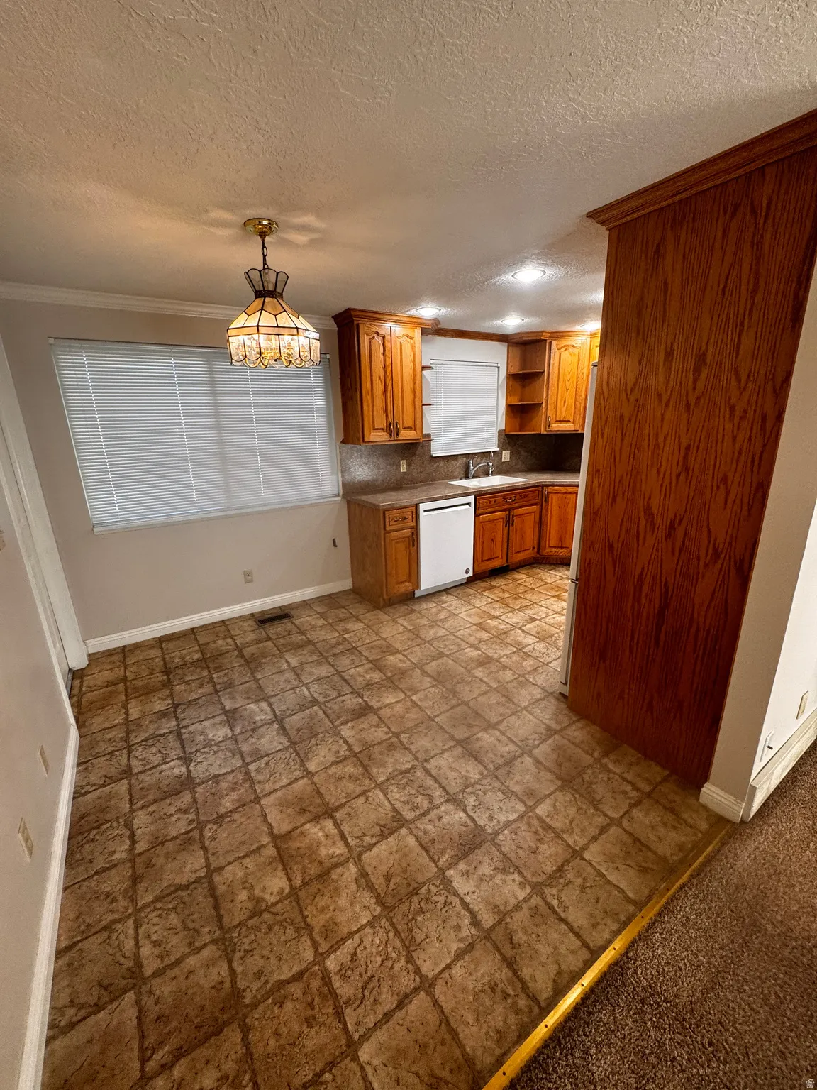 Kitchen area featuring a tiled floor, wood cabinetry, built-in dishwasher, recessed lighting, and a decorative pendant light fixture