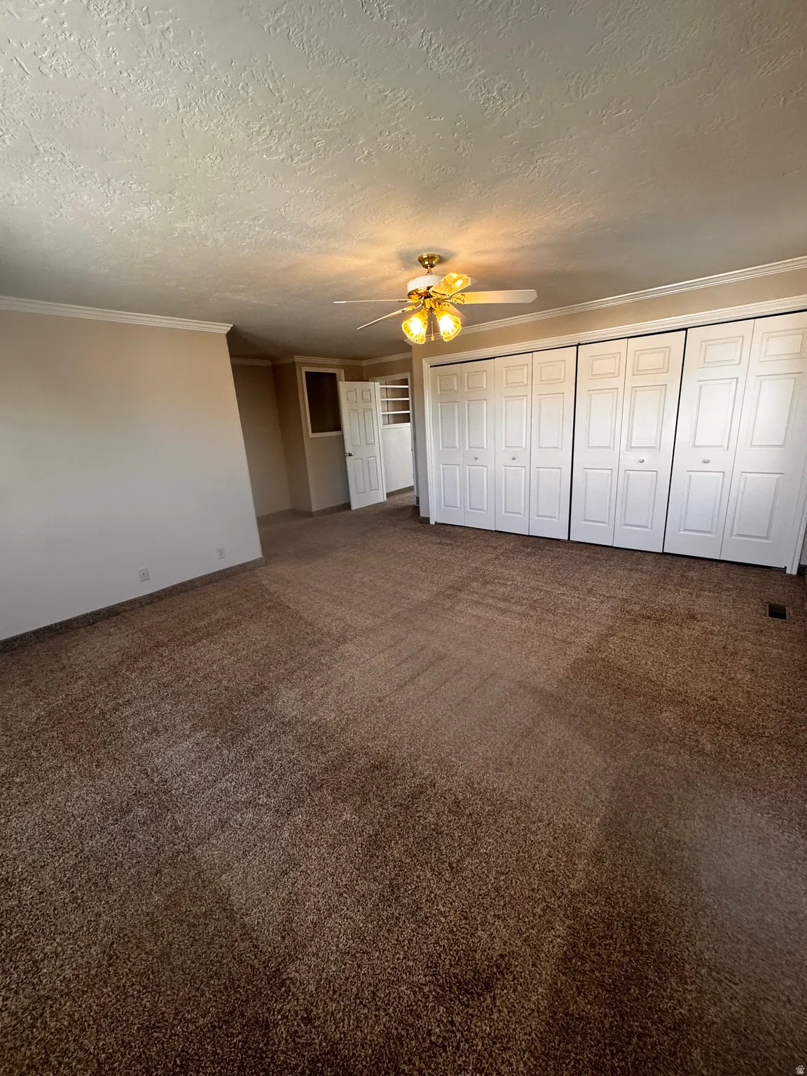 Room featuring broadloom carpet flooring, multiple bi-fold closet doors, a ceiling fan with integrated lighting, and crown molding details