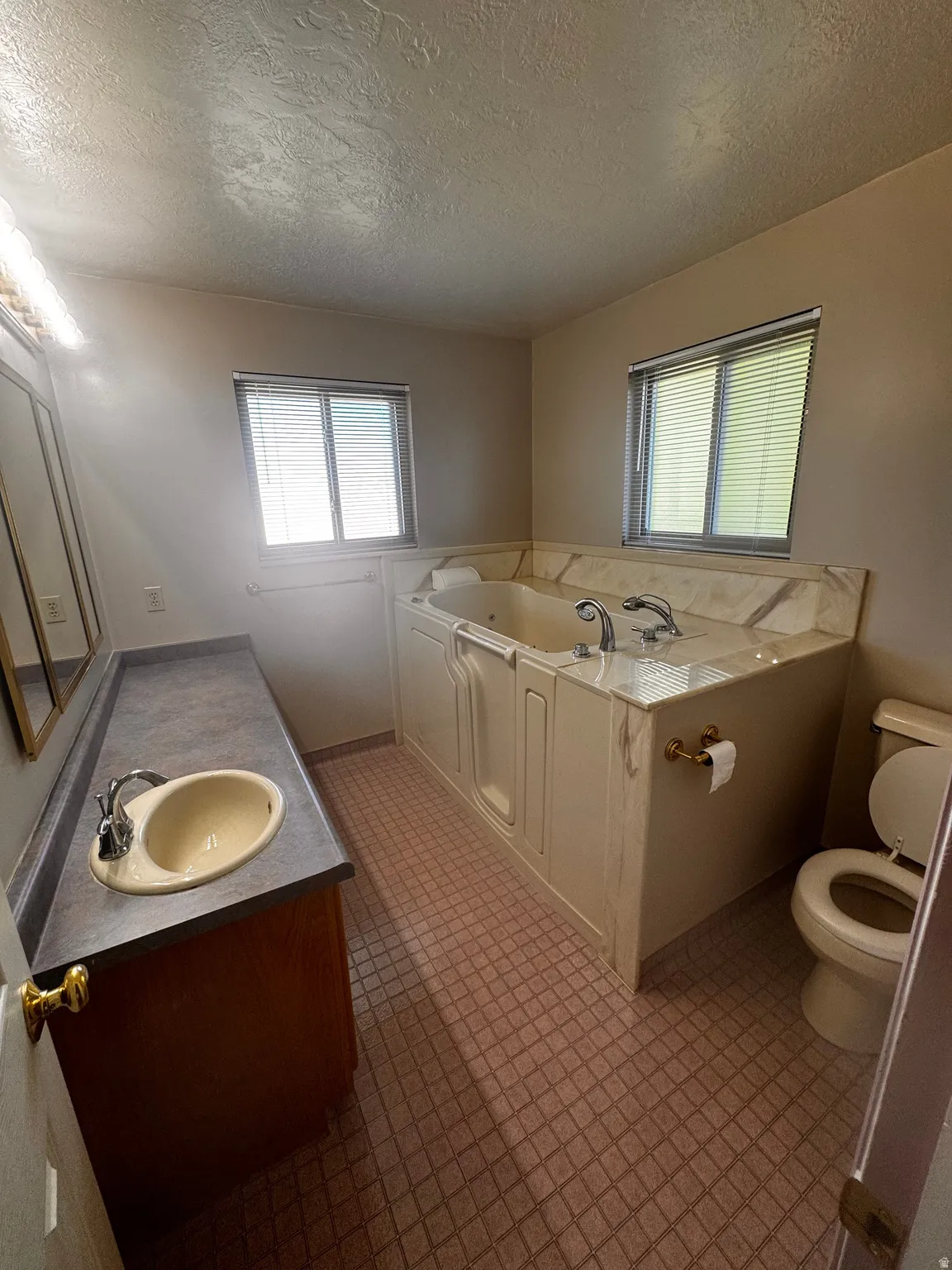 Bathroom featuring a built-in jetted tub, a single vanity with a laminate countertop, and a toilet