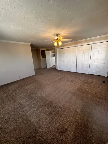 Room featuring broadloom carpet flooring, multiple bi-fold closet doors, a ceiling fan with integrated lighting, and crown molding details