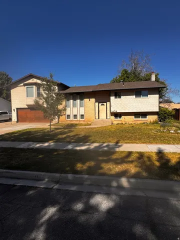 Split-level residence featuring a brown asphalt shingle roof and a two-car garage with a wood-finish door