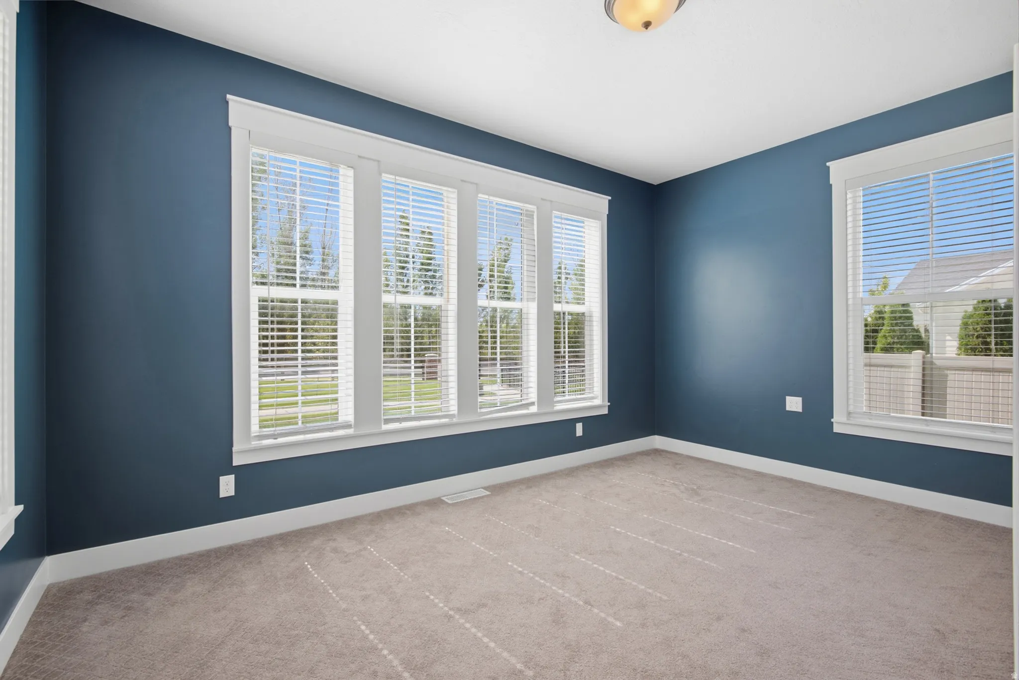 Bedroom 2 with carpeted flooring with a neutral finish, multiple windows with white blinds, white trim, and a ceiling-mounted light fixture