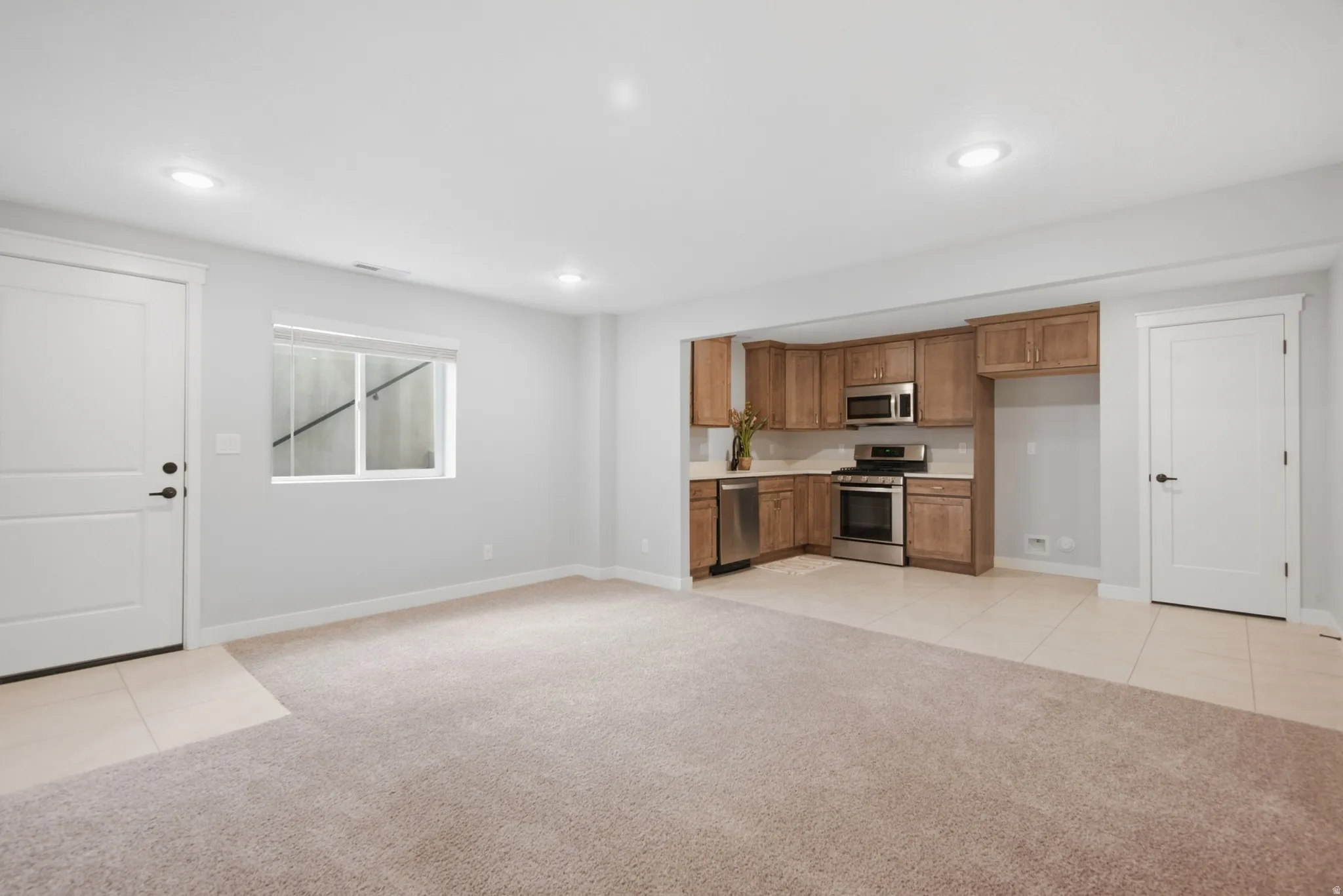 Basement ADU great room with walk-out access. Recessed lighting throughout, full kitchen with stainless steel appliances, wood-finish cabinetry, light-toned countertop, and light-toned flooring
