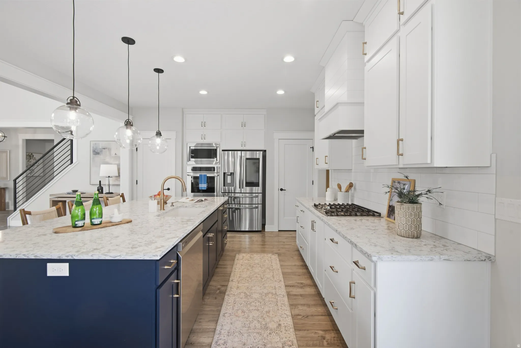 Kitchen featuring a large island with a deep blue base and light-toned countertop, white cabinetry with gold-toned hardware, stainless steel appliances, and wood-finish flooring