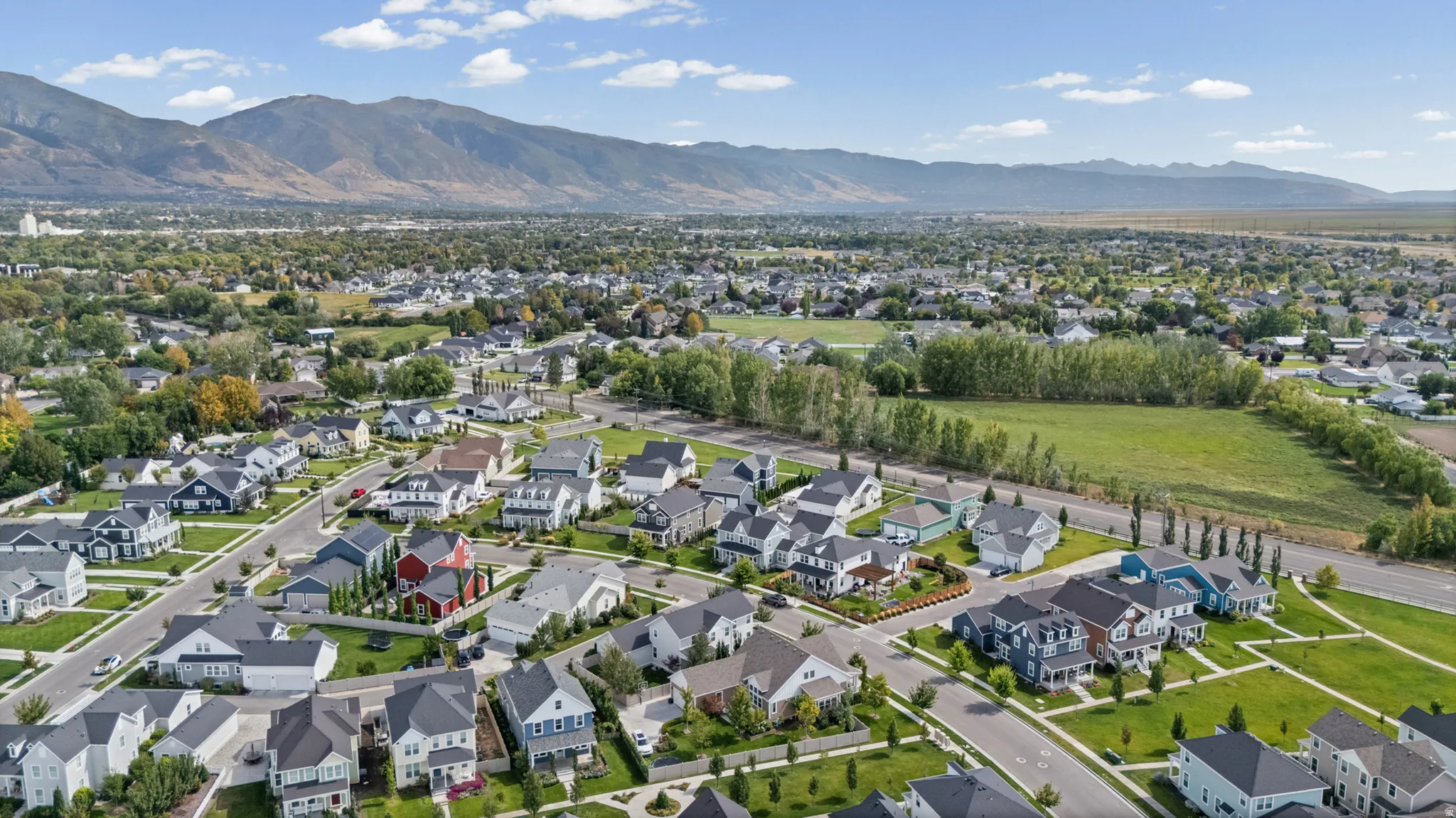 Residential neighborhood with paved streets and sidewalks, surrounded by mature trees, green spaces, and distant mountains