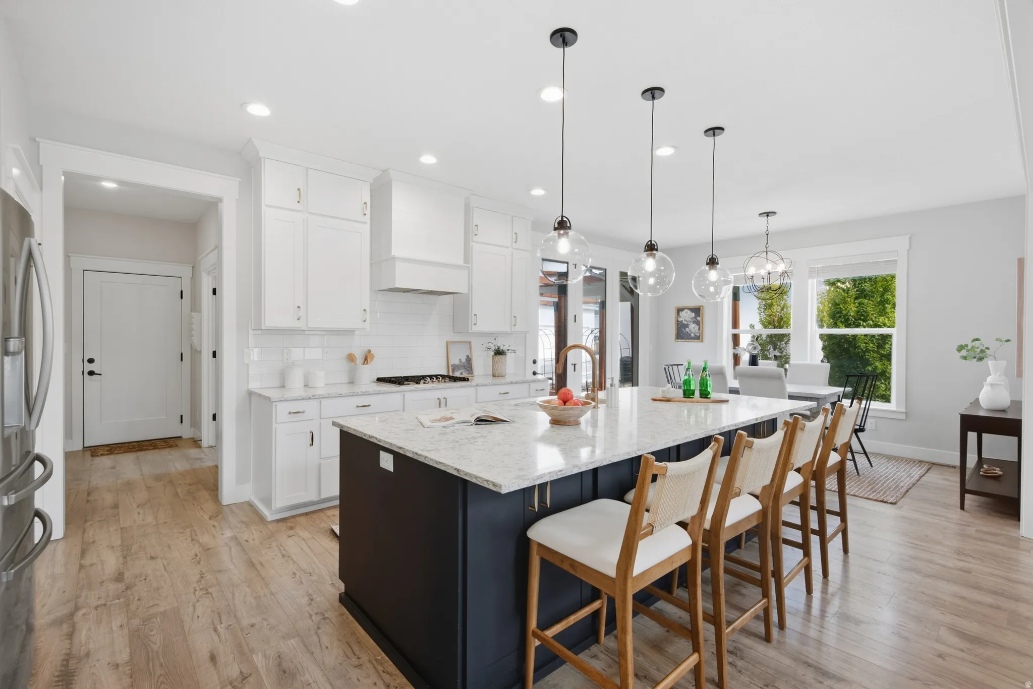 Wood-finish flooring throughout, white cabinetry, a dark-toned kitchen island with a light-toned countertop, and multiple pendant lights