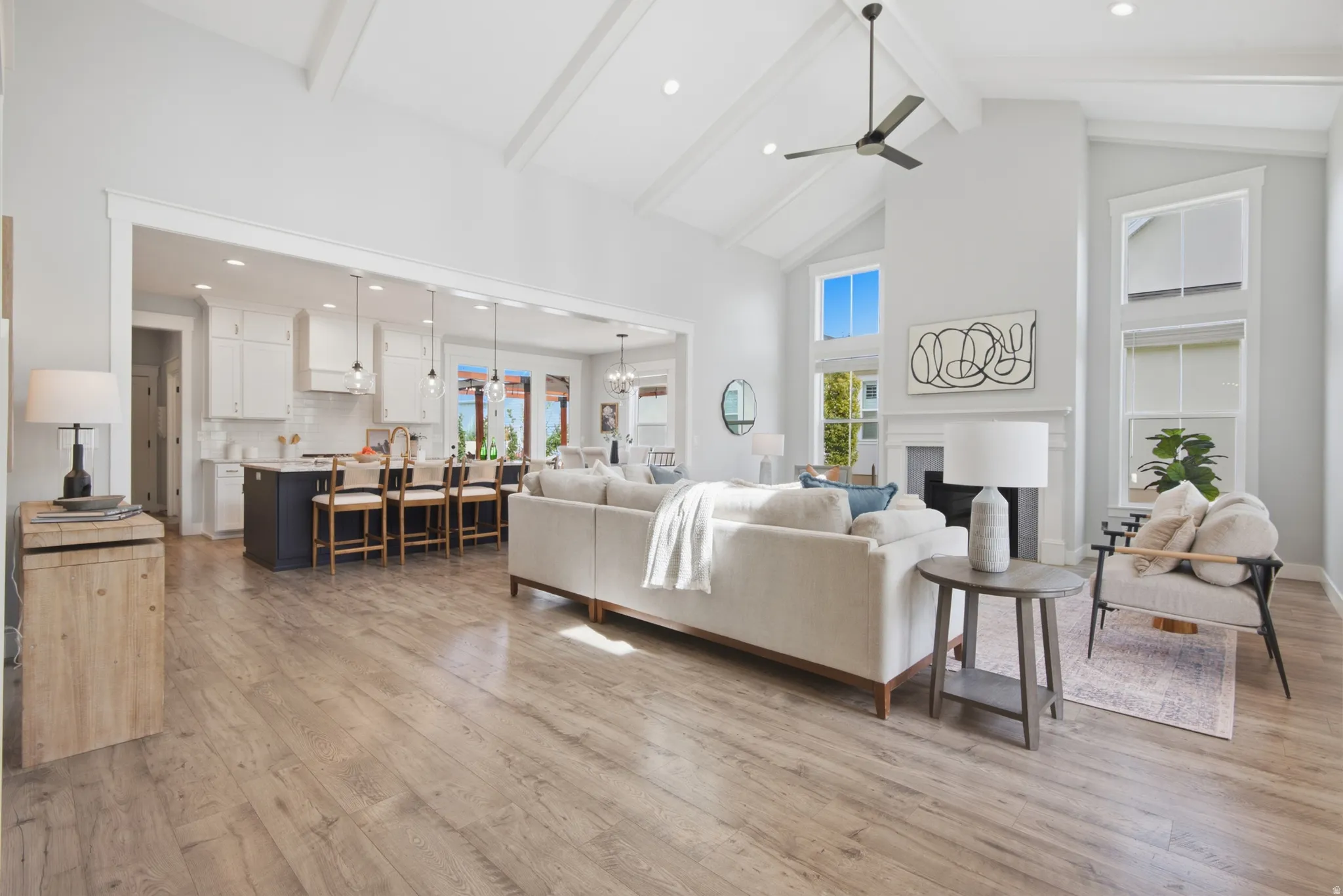Vaulted ceiling with exposed beams, wood-finish flooring, kitchen island with seating, pendant lighting, and a fireplace with a white mantel