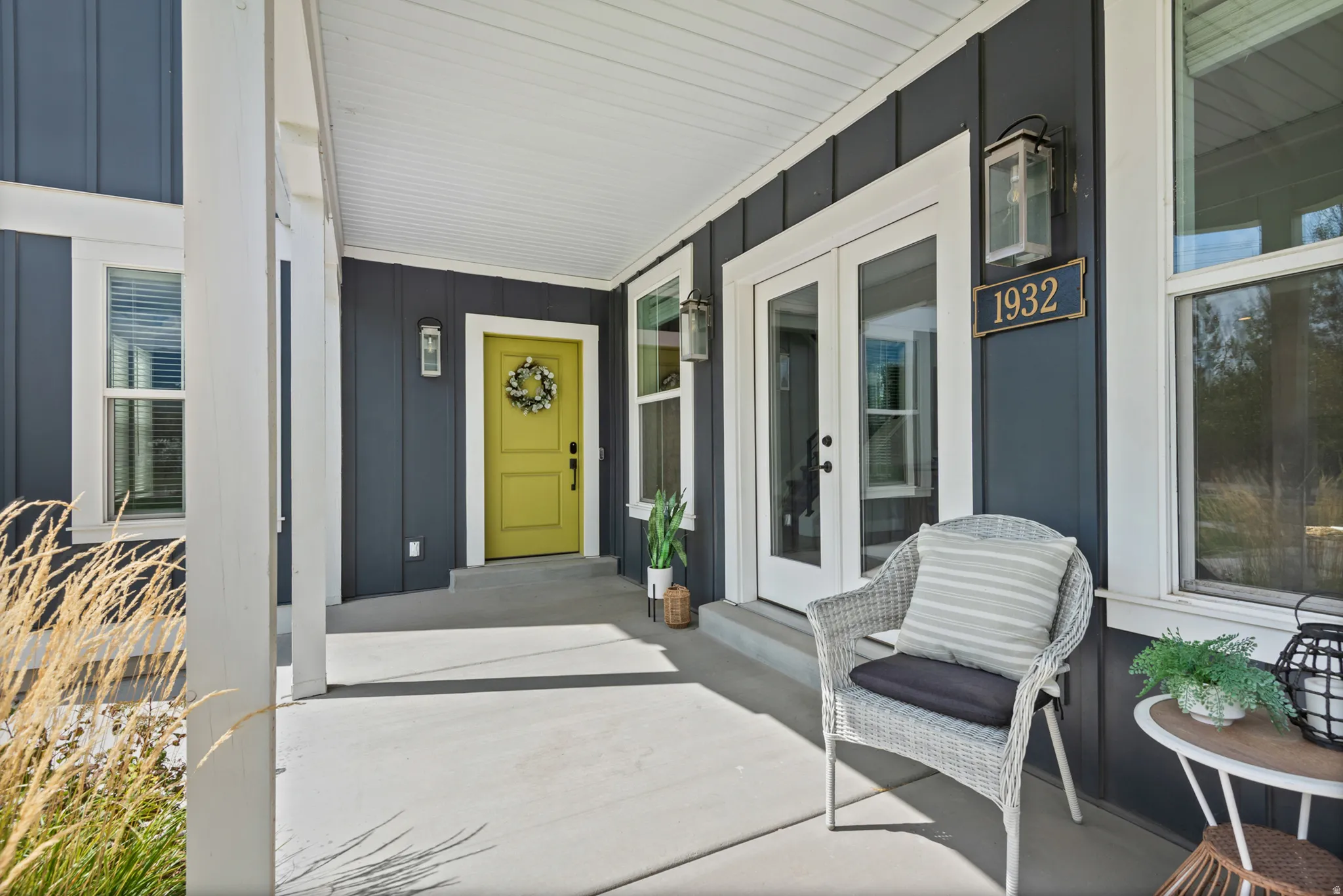 Covered porch featuring board and batten siding, multiple windows, a vibrant entry door, and double glass-paneled doors
