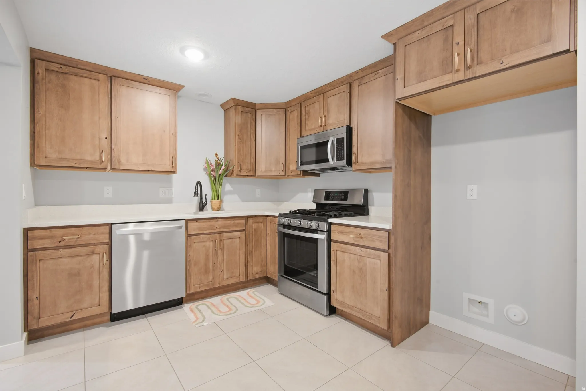 Basement ADU Kitchen featuring wood cabinetry, light countertops, stainless steel appliances, and tile flooring