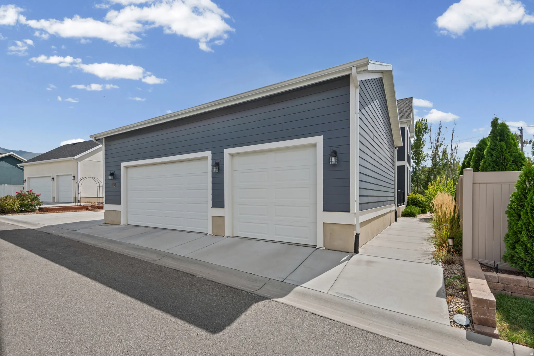 Three-car oversized garage (will fit a double cab full sized truck) with white doors, dark blue siding, and white trim, walkway to basement ADU