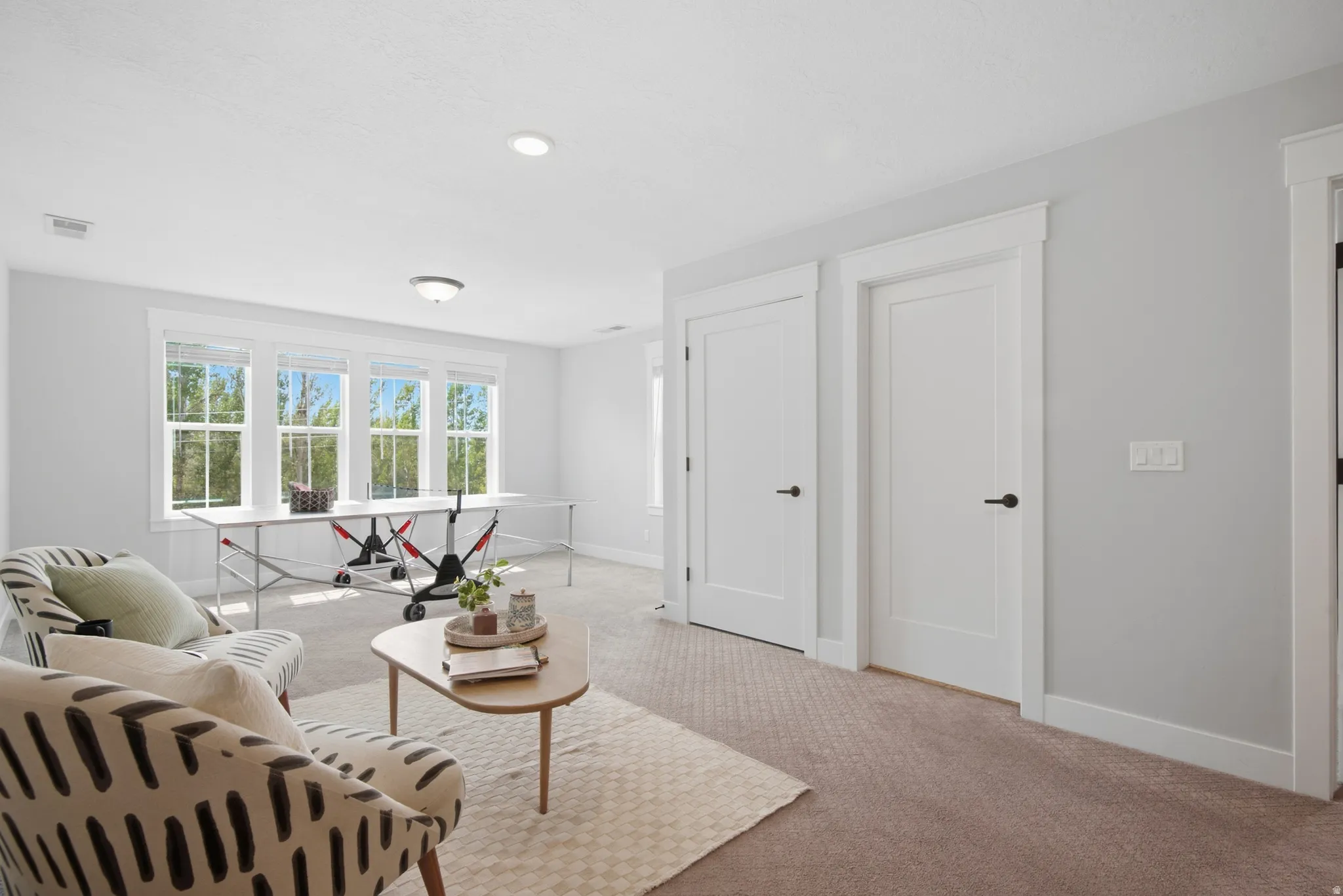 Recessed lighting, large windows, light gray wall paint, white trim, and light brown carpeting