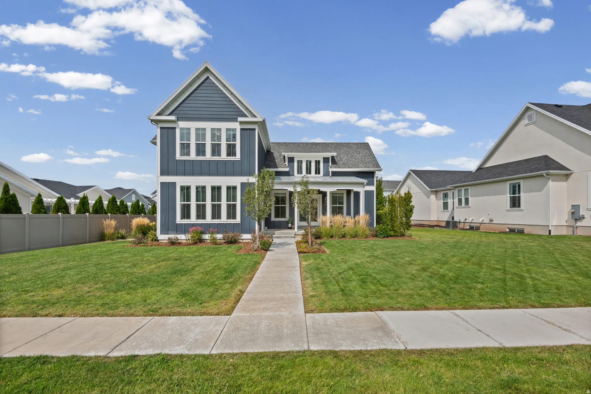 Exterior featuring blue siding, white window frames, a covered front porch, a concrete sidewalk, and a manicured lawn