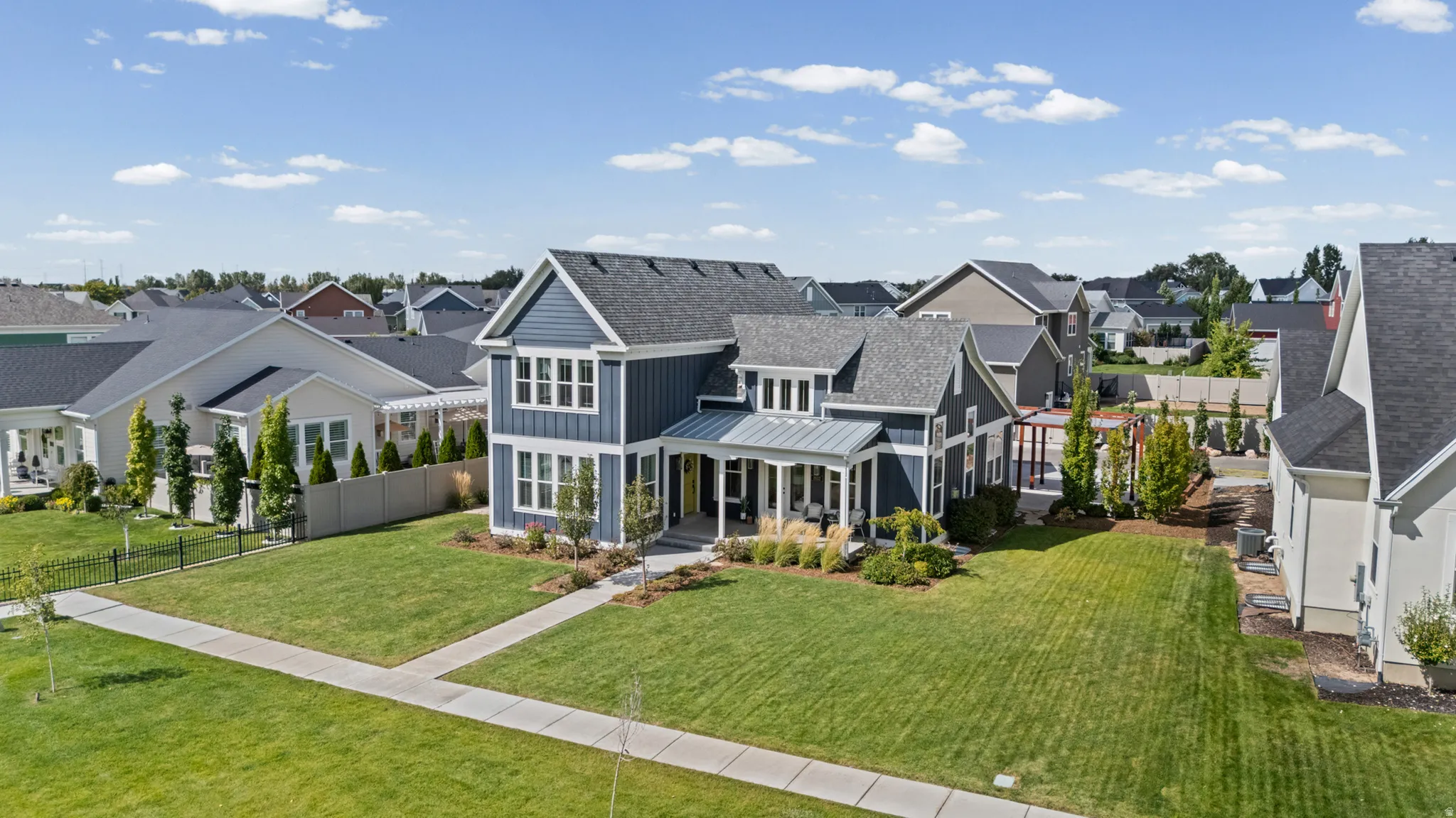 Contemporary two-story residence featuring a blue vertical siding façade with white trim, an inviting front porch with a standing seam metal roof, and a meticulously manicured lawn