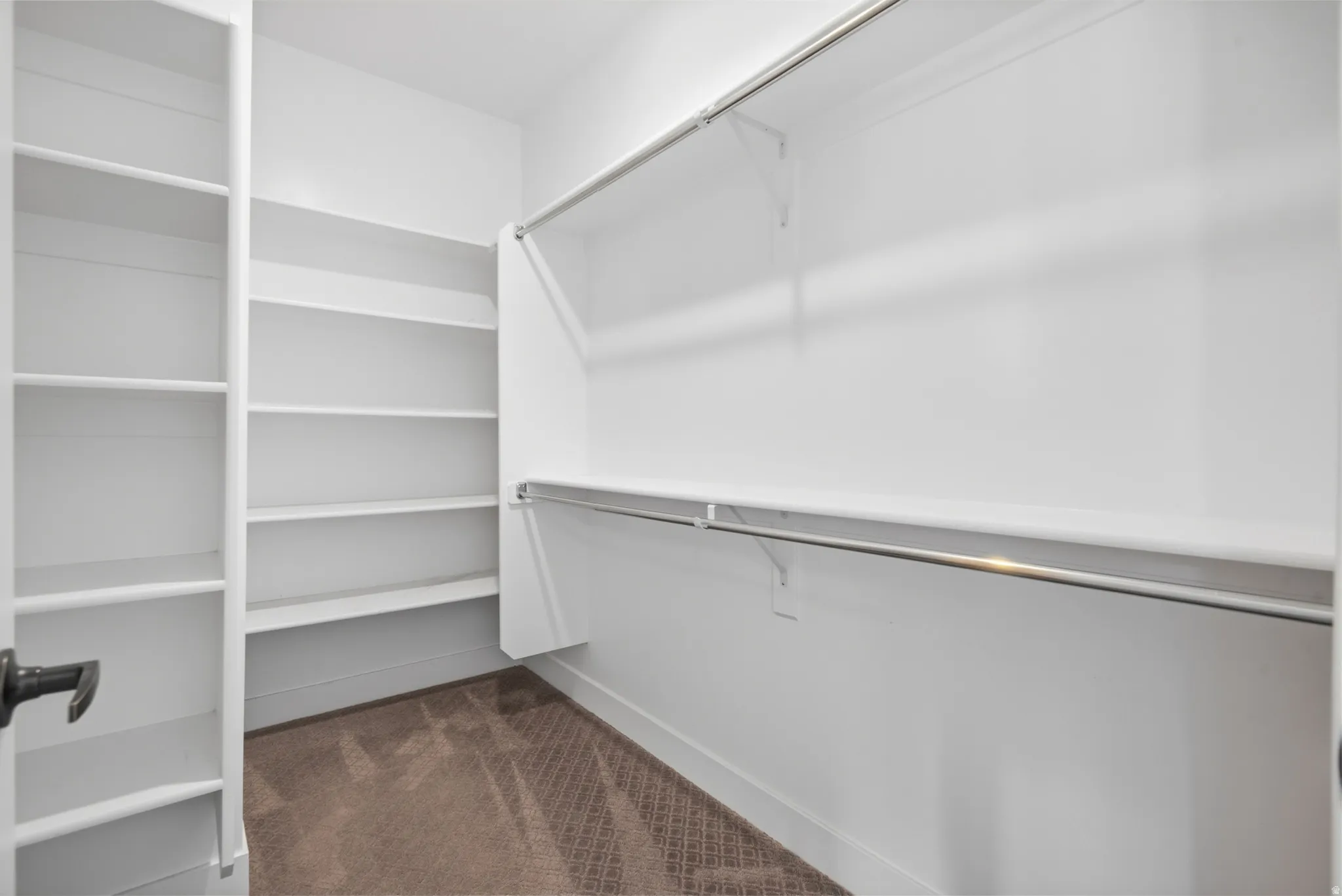 Primary Bedroom walk-in closet Built-in shelving, chrome hanging rods, and patterned carpeting