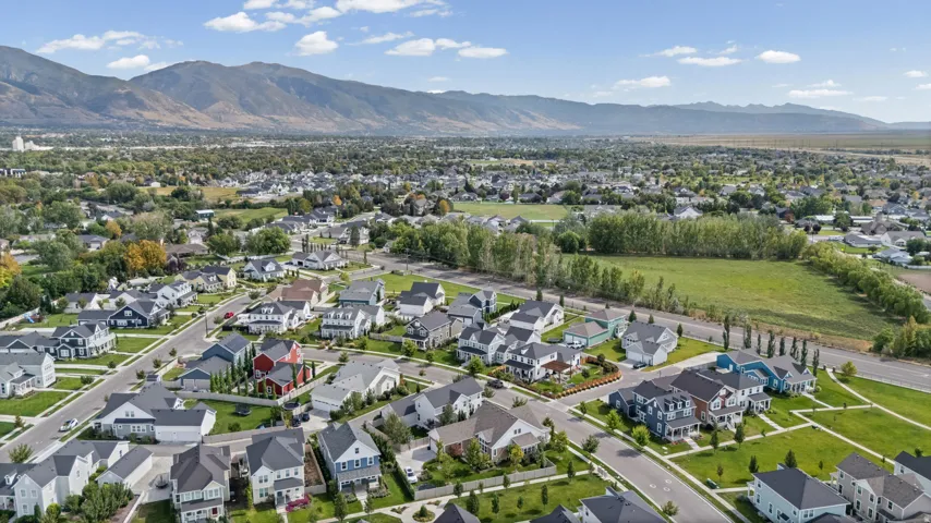 Residential neighborhood with paved streets and sidewalks, surrounded by mature trees, green spaces, and distant mountains