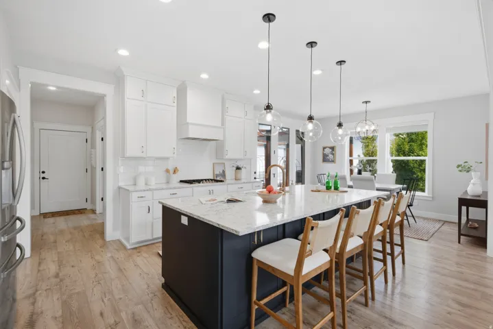 Wood-finish flooring throughout, white cabinetry, a dark-toned kitchen island with a light-toned countertop, and multiple pendant lights