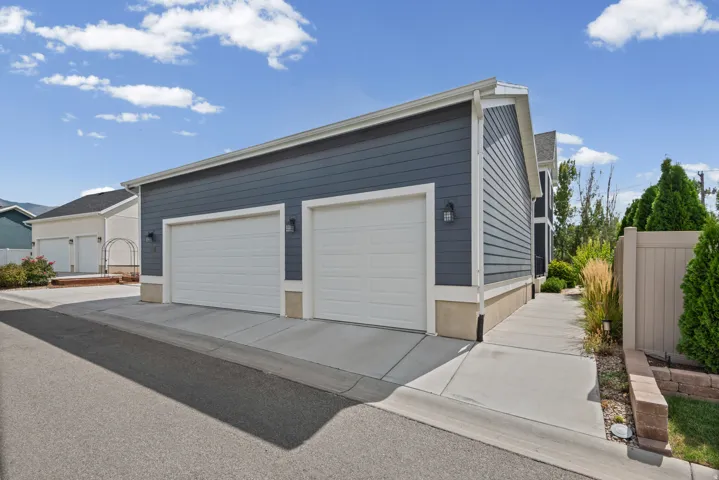 Three-car oversized garage (will fit a double cab full sized truck) with white doors, dark blue siding, and white trim, walkway to basement ADU