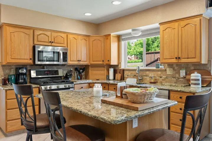 Kitchen featuring oak cabinetry, granite countertops, stainless steel appliances, a tiled backsplash, and an island with seating