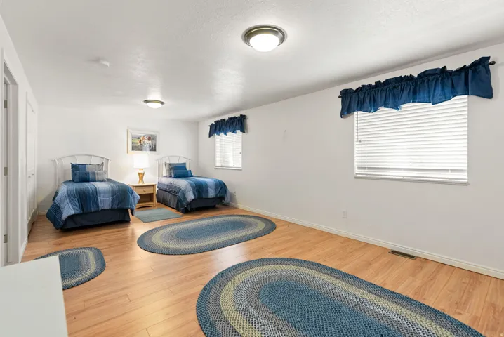 Spacious room featuring light wood-finish flooring, white walls, two windows with blinds, and recessed lighting fixtures