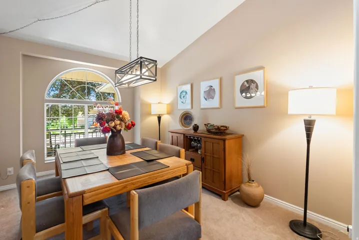 Carpeted dining area featuring a vaulted ceiling and an arched window