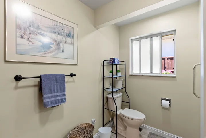 Primary bathroom featuring light-toned walls, a white-framed window with frosted glass, and a toilet with a metal etagere for storage