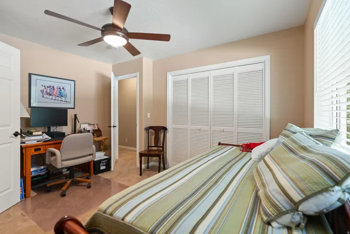 Bedroom featuring a ceiling fan with integrated lighting, louvered bi-fold closet doors, a built-in desk area, and window with horizontal blinds
