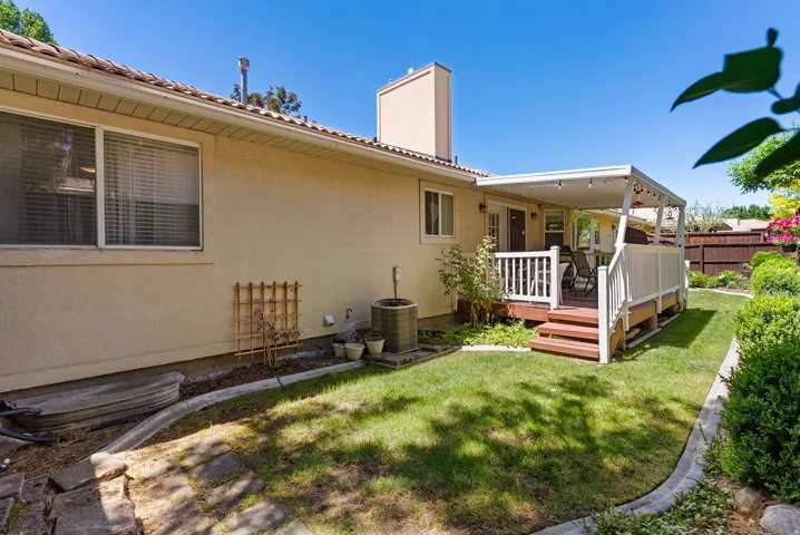 Expansive backyard featuring a covered patio, tiered deck with white railings, and a manicured lawn with established landscaping